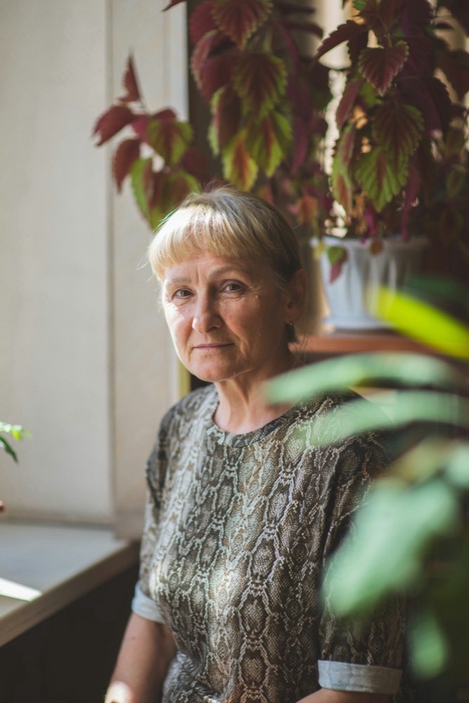 A woman standing by a window at home beside a large houseplant