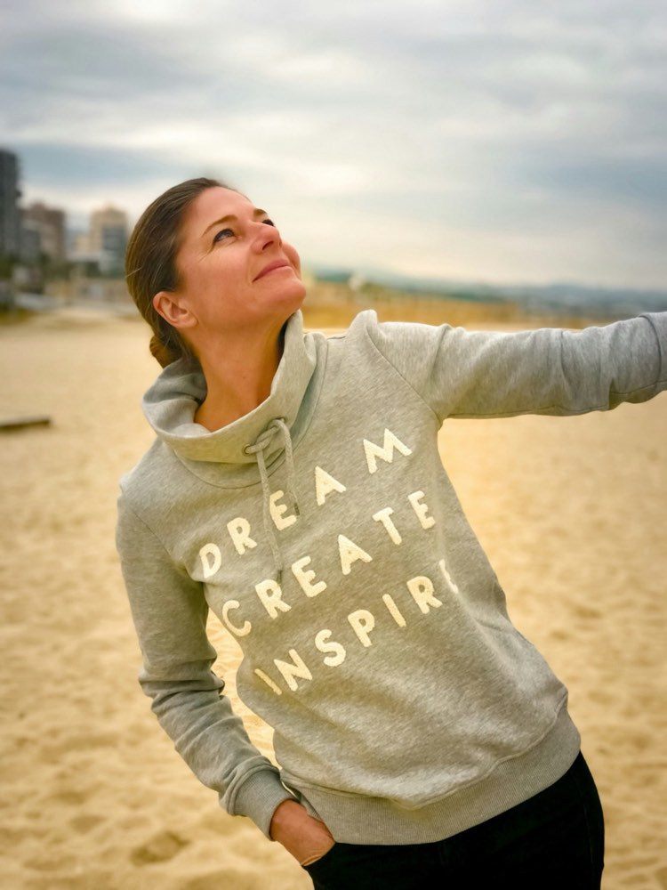 A woman on a beach with one arm outstretched, looking upward