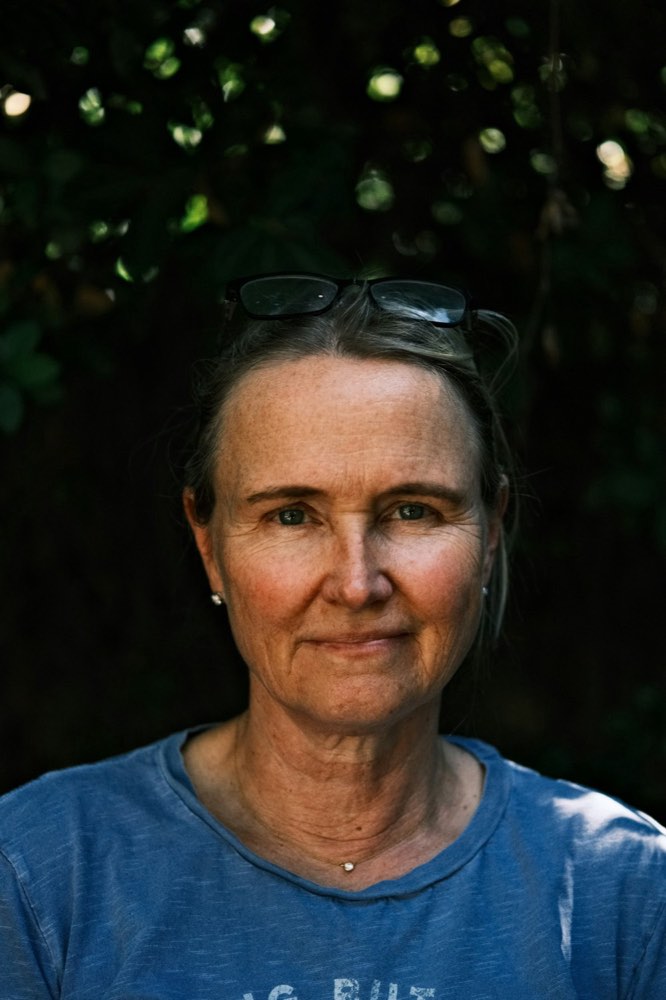 A woman in her late forties outdoors among greenery, smiling gently